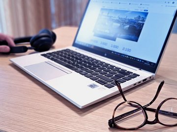 Lächelnde Frau mit langem braunen Haar in einem Büro sitzt vor ihrem Laptop.